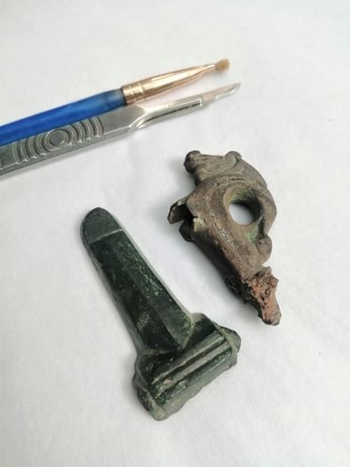 A Roman phallic object which is possibly a belt buckle cover. Its base white metal is plated with copper alloy. The object on the right is part of an Anglo Saxon stirrup mount. It is made of copper alloy with niello inlay.